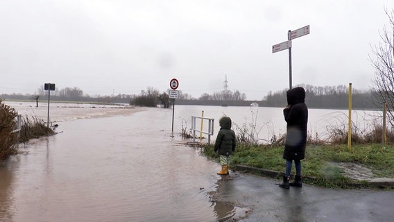 Eine Frau und ein Kind stehen vor einer überschwemmten Straße im Landkreis Northeim. © NonstopNews 