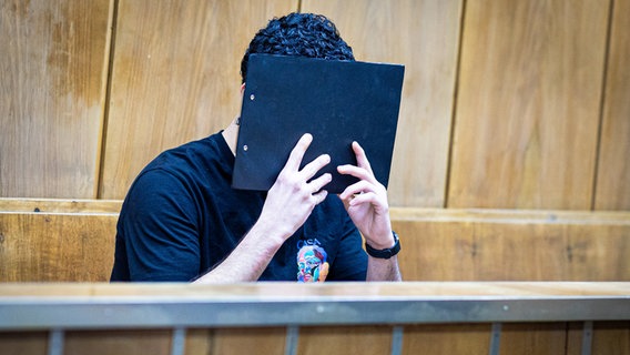 Der Angeklagte verdeckt sein Gesicht mit einer Mappe bei Prozessauftakt in einem Saal im Landgericht Hannover. © dpa-picture alliance Foto: Moritz Frankenberg