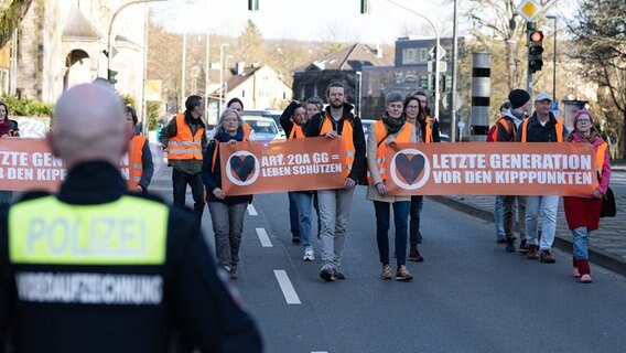 Aktivisten der Bewegung «Letzte Generation» gehen mit Plakaten bei einem Protestmarsch über eine Hauptverkehrsstraße. © Swen Pförtner/dpa Foto: Swen Pförtner
