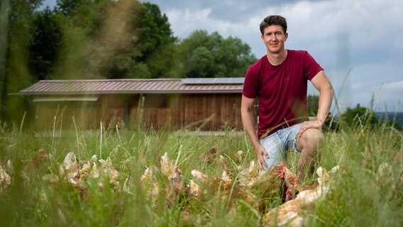 Junglandwirt Stefan Golze aus Dassel aus dem Landkreis Northeim hockt neben seinen Hühnern im Gras. © Timo Jaworr für agrarheute Foto: Timo Jaworr für agrarheute