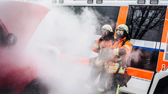 Zwei Feuerwehrleute mit Atemschutzmasken löschen einen Brand. © NDR Foto: Julius Matuschik