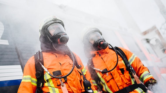 Zwei Feuerwehrleute mit Atemschutzmasken stehen in dichtem Rauch. © NDR Foto: Julius Matuschik