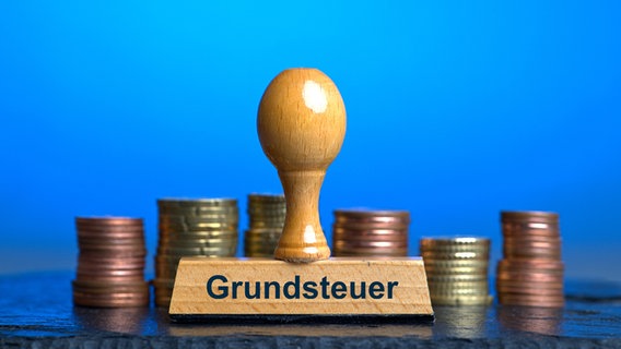 Ein Holzstempel mit der Aufschrift "Grundsteuer" steht vor mehreren Stapeln mit Euro. © picture alliance/SULUPRESS.DE/Torsten Sukrow Foto: Torsten Sukrow