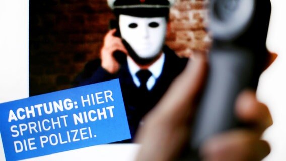Ein Telefonhörer ist vor einem Plakat der Polizei NRW mit der Aufschrift «Achtung: Hier spricht nicht die Polizei» zu sehen. © PictureAlliance 