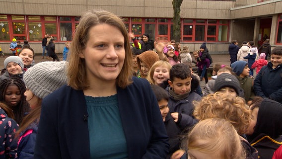 Kultusministerin Julia Willie Hamburg ist  auf einem Schulhof umringt von Kindern. © NDR 