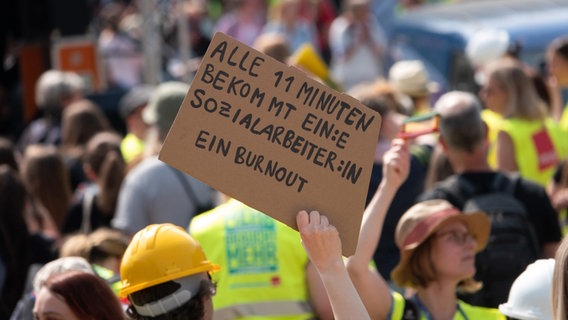 Eine Frau hält ein Schild mit der Aufschrift "Alle 11 Minuten bekommt ein:e Sozialarbeiter:in ein Burnout" auf einer Kundgebung mehrerer Gewerkschaften auf dem Opernplatz in Hannover. © dpa/picture-alliance Foto: Mia Bucher