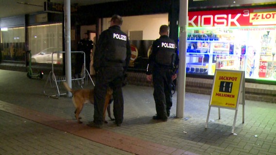 Einsatzkräfte der Polizei und ein Spürhund stehen während einer Kontrollaktion gegen illegales Glücksspiel vor einem Kiosk in der Region Hannover. © dpa 