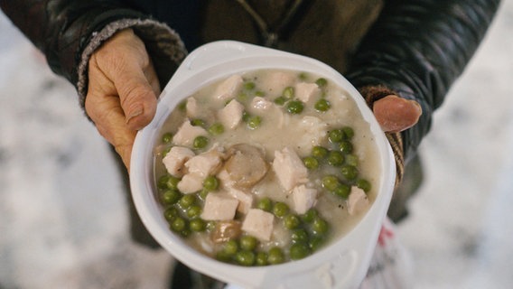 Eine obdachlose Frau hält eine warme Mahlzeit des Johanniter-Kältebus in den Händen. © dpa Foto: Ole Spata