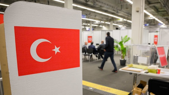 Ein Wahlkabine mit einer Flagge steht in einem Wahllokal für die türkische Präsidentschaftswahl in der Messe Hannover. © Julian Stratenschulte/dpa Foto: Julian Stratenschulte