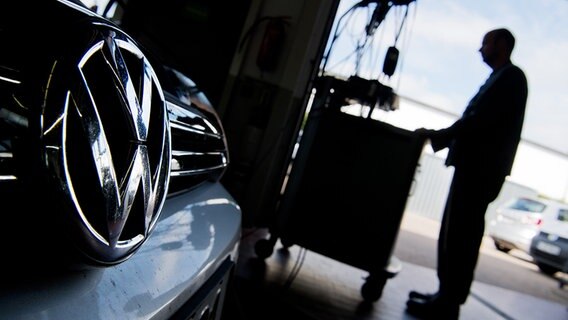 In einer Werkstatt sind der Kühlergrill eines Volkswagens und ein Kfz-Mechaniker im Gegenlicht zu sehen. © picture alliance/dpa Foto: Julian Stratenschulte