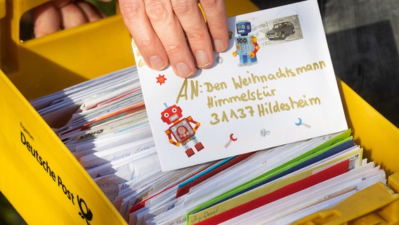 Ein Mann hält einen an den Weihnachtsmann adressierten Brief in der Hand. Darunter eine Kiste weiterer Briefe. © picture alliance/dpa/Julian Stratenschulte Foto: Julian Stratenschulte