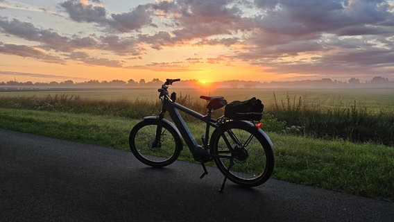 Ein Fahrrad vor weiter Landschaft bei Sonnenaufgang. © NDR Foto: Dirk Hessel