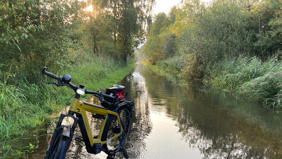 Ein E-Bike steht auf einem vom Regen überfluteten Weg an der Schleuse Sülfeld des Mittellandkanals. © NDR Foto: Holger Bartels