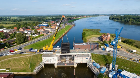 Mit einem Kran wird eines von zwei jeweils rund 40 Tonnen schweren Stemmtore im Ilmenau-Sperrwerk eingesetzt (Aufnahme mit einer Drohne). © dpa-Bildfunk Foto: Philipp Schulze/dpa