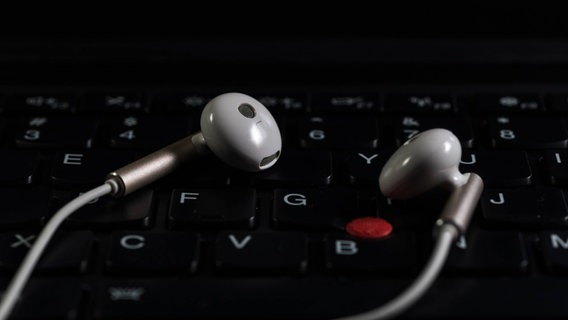 Kopfhörer liegen auf der Tastatur eines Laptops. © imago images/Imaginechina-Tuchong 