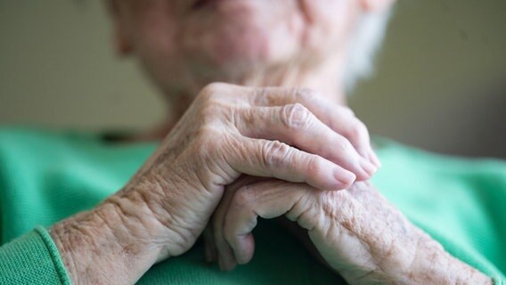 Eine Seniorin mit grünem Pullover faltet ihre Hände. © Marijan Murat/dpa Foto: Marijan Murat/dpa
