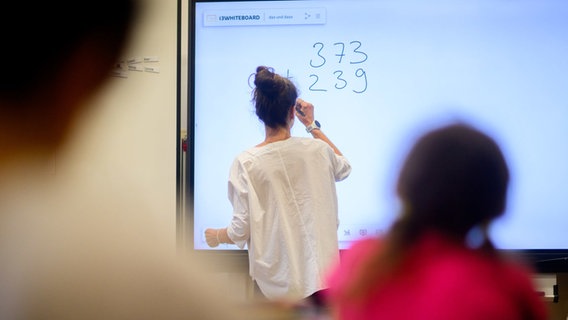Eine Lehrerin steht in einem Klassenzimmer an einer Tafel. © dpa Foto: Julian Stratenschulte