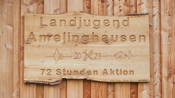 Auf einer Holztafel an einer Schutzhütte in Kronsbergheide in der Lüneburger Heide steht die Aufschrift "Landjugend Amelinghausen - 72 Stunden Aktion". © dpa-Bildfunk Foto: Georg Wendt