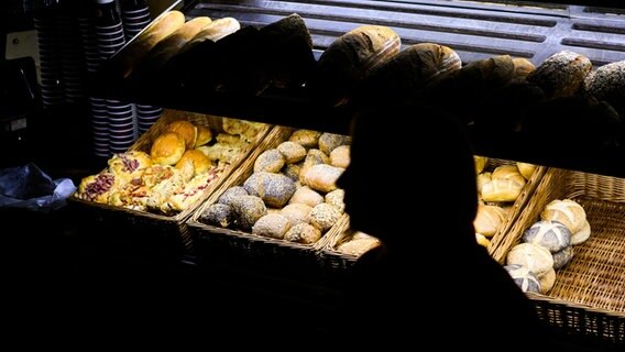 Eine Bäckereifachverkäuferin steht am frühen Morgen in der bewusst sparsam beleuchteten Bäckerei Fahrenhorst. © dpa Foto: Julian Stratenschulte