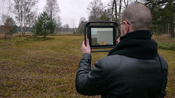 Ein Historiker hält ein iPad hoch und testet das Bergen-Belsen-App. © NDR Foto: Vassili Golod