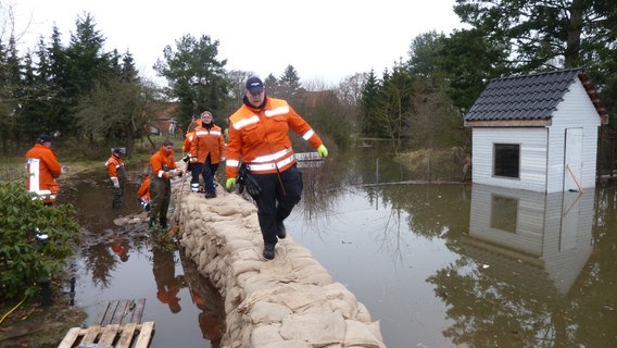 Feuerwehrleute gehen über einen Schutzdamm aus Sandsäcken.  Foto: Lars Gröning