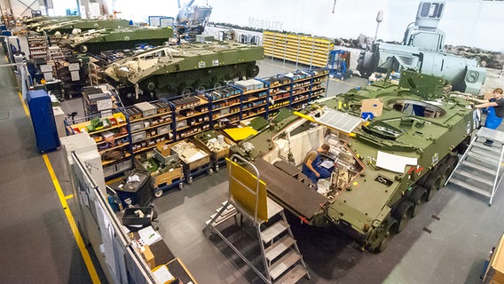 Mehrere Mitarbeiter der Rheinmetall AG arbeiten in einer Fabrikhalle an Panzern. © dpa Foto: Philipp Schulze