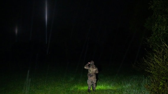 Mehrere Skybeamer leuchten in den Nachthimmel von Bremervörde, während ein Soldat Ausschau nach dem vermissten Jungen hält. © Jonas Walzberg / dpa Foto: Jonas Walzberg