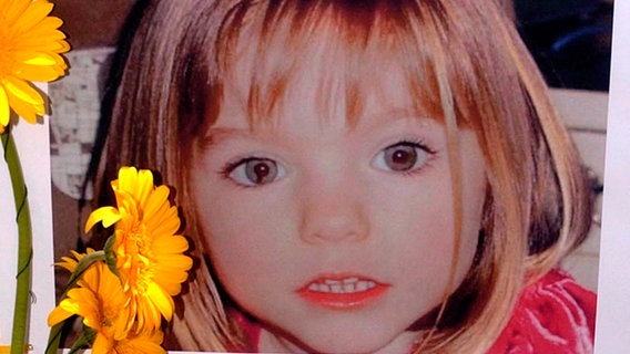 Blumen stehen vor einem Bild, das die verschwundene Madeleine McCann (Maddie) auf einem Foto zeigt, das ihre Eltern im Zusammenhang mit dem Verschwinden des Kindes veröffentlich haben. © picture alliance/dpa/LUSA/epa | Luis Forra Foto: Luis Forra