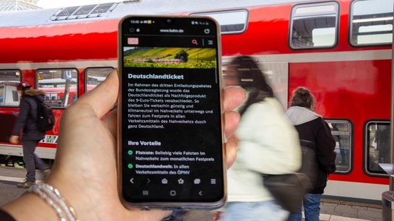 Nahaufnahme eines Smartphones vor ein- und aussteigenden Fahrgästen beim Halt eines Zuges ©  picture alliance / CHROMORANGE Foto: Udo Herrmann