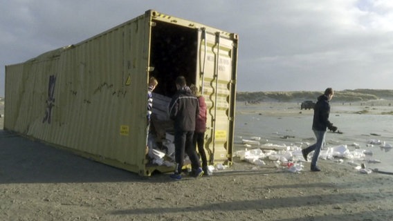 Menschen machen sich an am Strand liegenden Containern zu schaffen. © NDR Foto: André Steffens