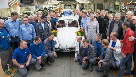 Arbeiter von VW gruppieren sich um einen weißen VW-Käfer.  Foto: VW Emden