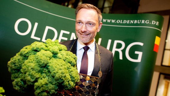 Der neue Oldenburger Grünkohlkönig Christian Lindner (FDP), Bundesfinanzminister, trägt eine Kohlkette und hält eine Grünkohlpflanze in den Händen. © dpa-Bildfunk Foto: Hauke-Christian Dittrich
