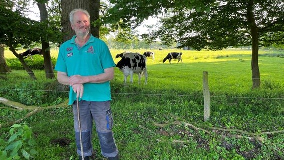 Ein Mann steht vor einer Kuh-Weide. Im Hintergrund grasen einige Tiere. © Catherine Grim/NDR Foto: Catherine Grim