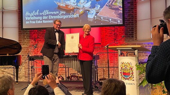 Eske Nannen bekommt auf einer Bühne die Ehrenbürgerschaft der Stadt Emden von Oberbürgermeister Tim Kruithoff (parteilos) verliehen. © NDR Foto: Nadia Yaqub