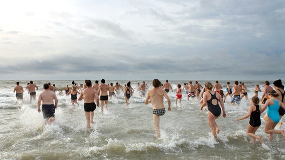 Männer, Frauen und Kinder laufen beim Neujahrsschwimmen auf Borkum ins Meer. © dpa/lni Foto: Reinhold Grigoleit