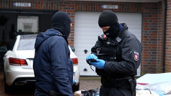 Zwei Spezialkräfte der Polizei stehen nach einer Razzia vor einem Haus in Lohne. © Nord-West-Media TV 
