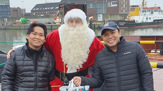 Ein Weihnachtsmann steht zwischen zwei Arbeitern für die Seefahrt. © Deutsche Seemannsmission Cuxhaven 