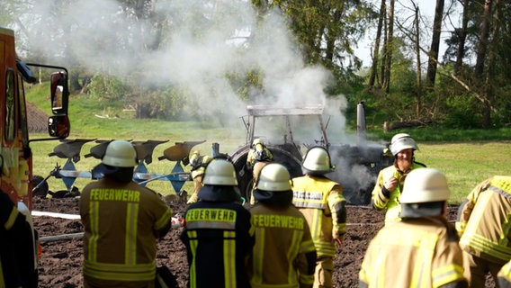 Feuerwehrleute stehen vor einem ausgebrannten Traktor in Groß Ippener. © Nord-West-Media TV 