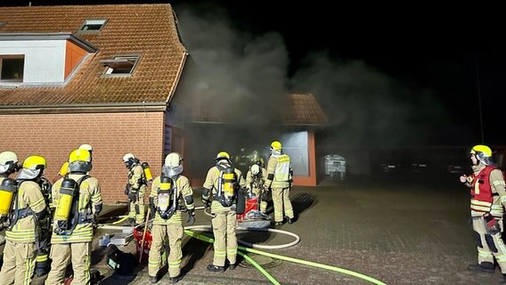 Feuerwehrleute stehen nach einem Brand in Langwedel (Landkreis Verden) an einem Haus, aus dem Rauch steigt. © Kreisfeuerwehr Verden/Dennis Köhler Foto: Dennis Köhler