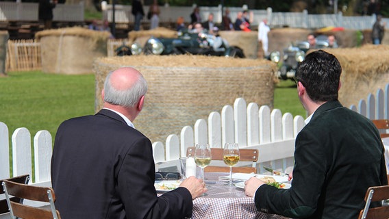 Zwei Männer im Anzug beobachten bei einem Glas Wein die Vintage Race Days. © NDR Foto: Olliver Gressieker