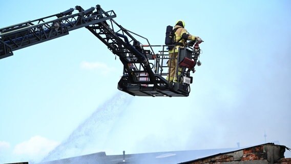 Ein Feuerwehrmann löscht von einer Drehleiter aus. Bei einem Großbrand in einem Werkstattgebäude in Wilhelmshaven ist ein Mensch ums Leben gekommen. © Lars Klemmer/dpa Foto: Lars Klemmer