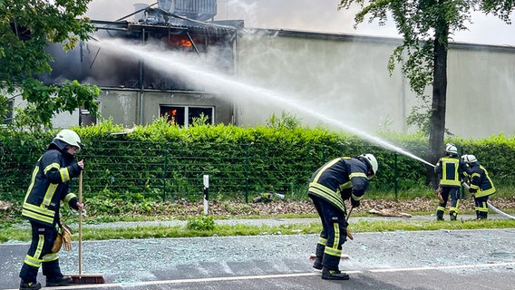 Feuerwehrleute löschen einen Brand in Dalum, während andere Glassplitter von der Straße fegen. © Nord-West-Media TV 