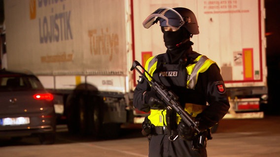 Ein schwer bewaffneter Polizist steht auf einem Autobahnparkplatz. © NDR 