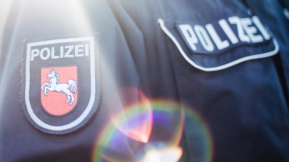 Auf dem mit Gegenlicht fotografiertem Jackenärmel einer Polizeiuniform ist das niedersächsischen Wappen aufgenäht. © NDR Foto: Julius Matuschik