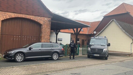 Spezialeinsatzkräfte der Polizei stehen mit zwei Einsatzfahrzeugen für eine Razzia zu Reichsbürgern vor einem Hof. © NDR 