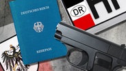 Ein Reichsbürger-Pass liegt neben einer Waffe und einem Nummernschild. © picture alliance/Christian Ohde Foto: Christian Ohde