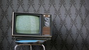 Alter Fernseher aus den 60er Jahren auf einem Hocker vor Mustertapete. © fotolia.com Foto: p!xel 66