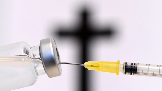 Eine Spritze wird aufgezogen, im Hintergrund ein schwarzes Kreuz. (Themenbild) © picture alliance/APA/picturedesk.com Foto: Helmut Fohringer