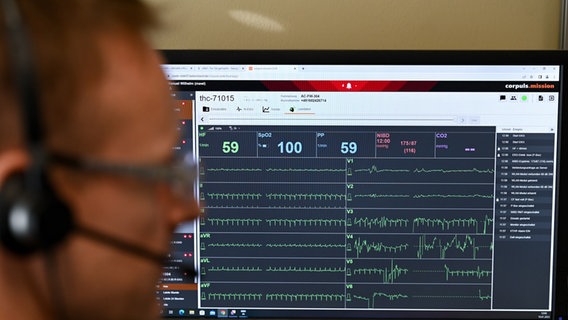 Ein Mediziner mit Headset sitzt vor einem Bildschirm auf dem Vitalwerte angezeigt werden. © picture alliance/dpa Foto: Arne Dedert