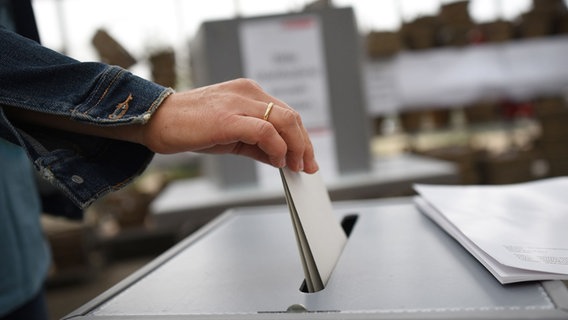 Eine Hand hält einen Wahlzettel und steckt diesen in den Schlitz einer Wahlurne. © picture alliance Foto: Henning Kaiser